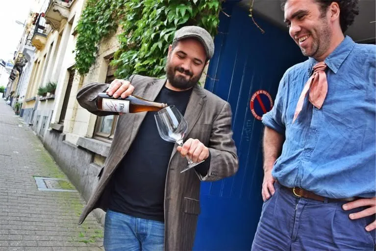 Twee brouwers van L'Annexe schenken een bier uit voor de blauwe deur van de brouwerij
