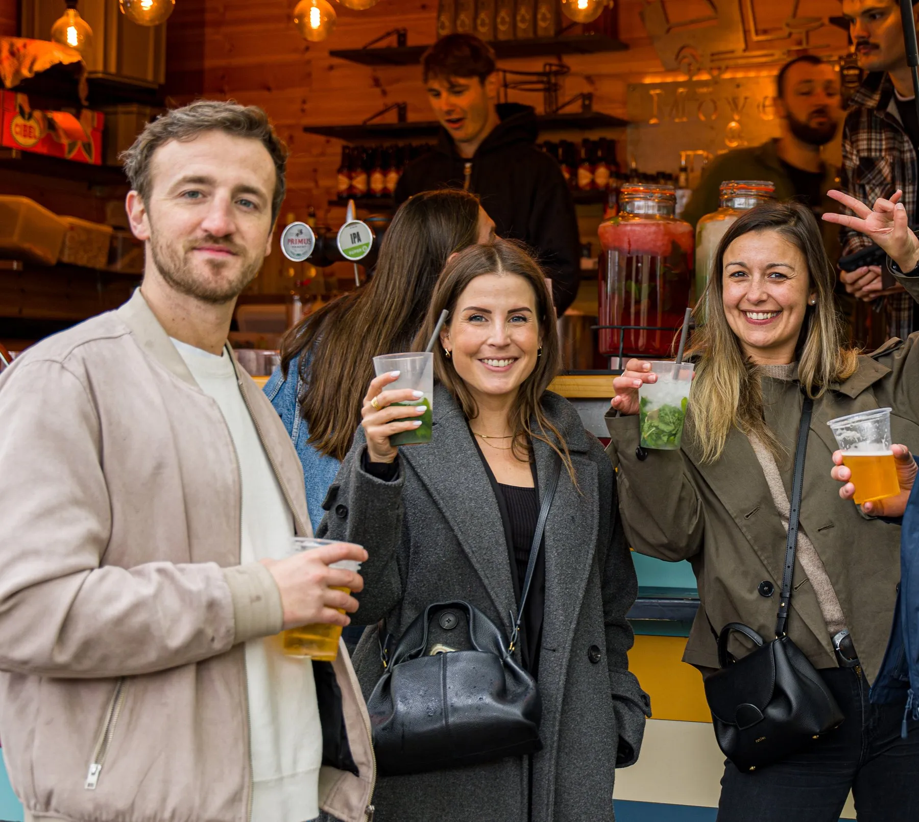 Quatre visiteurs lèvent leurs mojitos et leurs bières devant le bar
