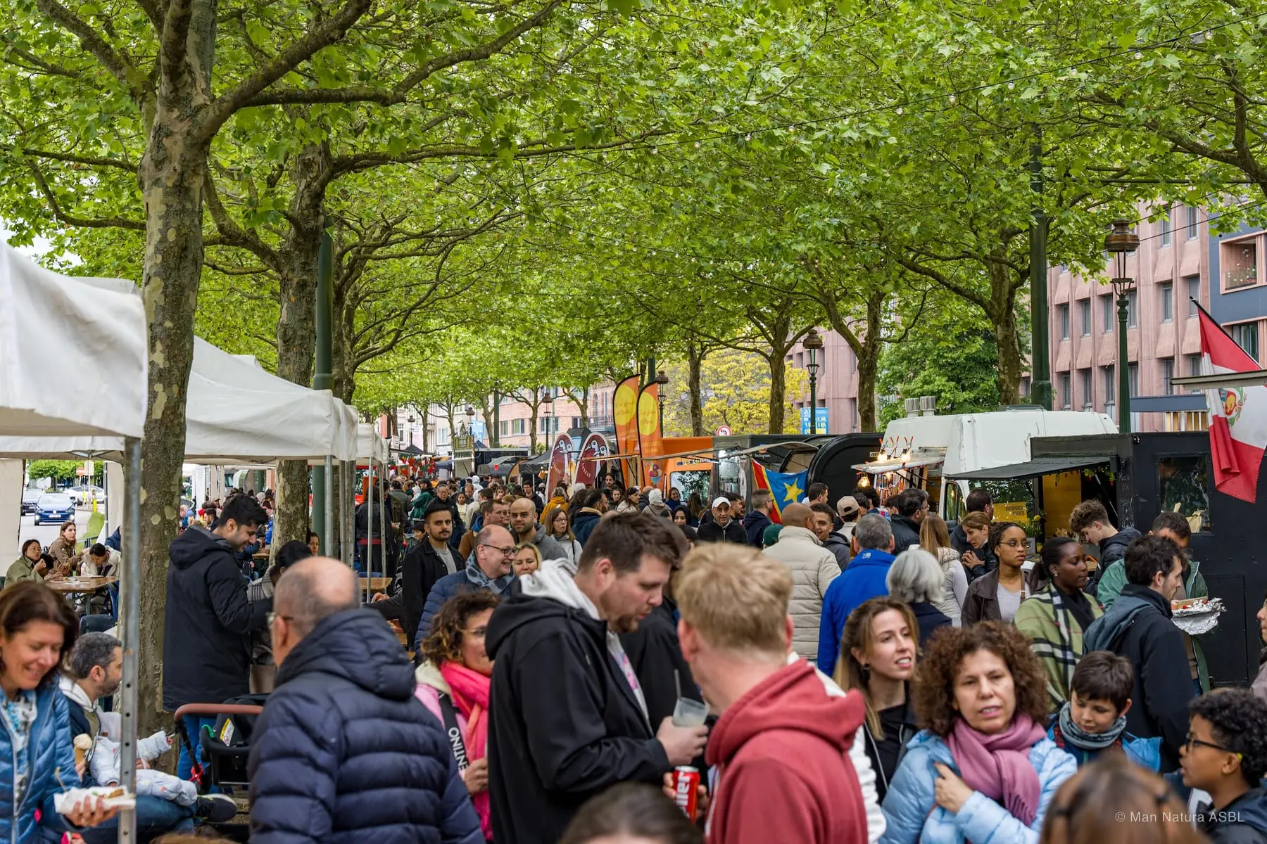 La foule circule entre les stands sous les platanes du Boulevard du Souverain