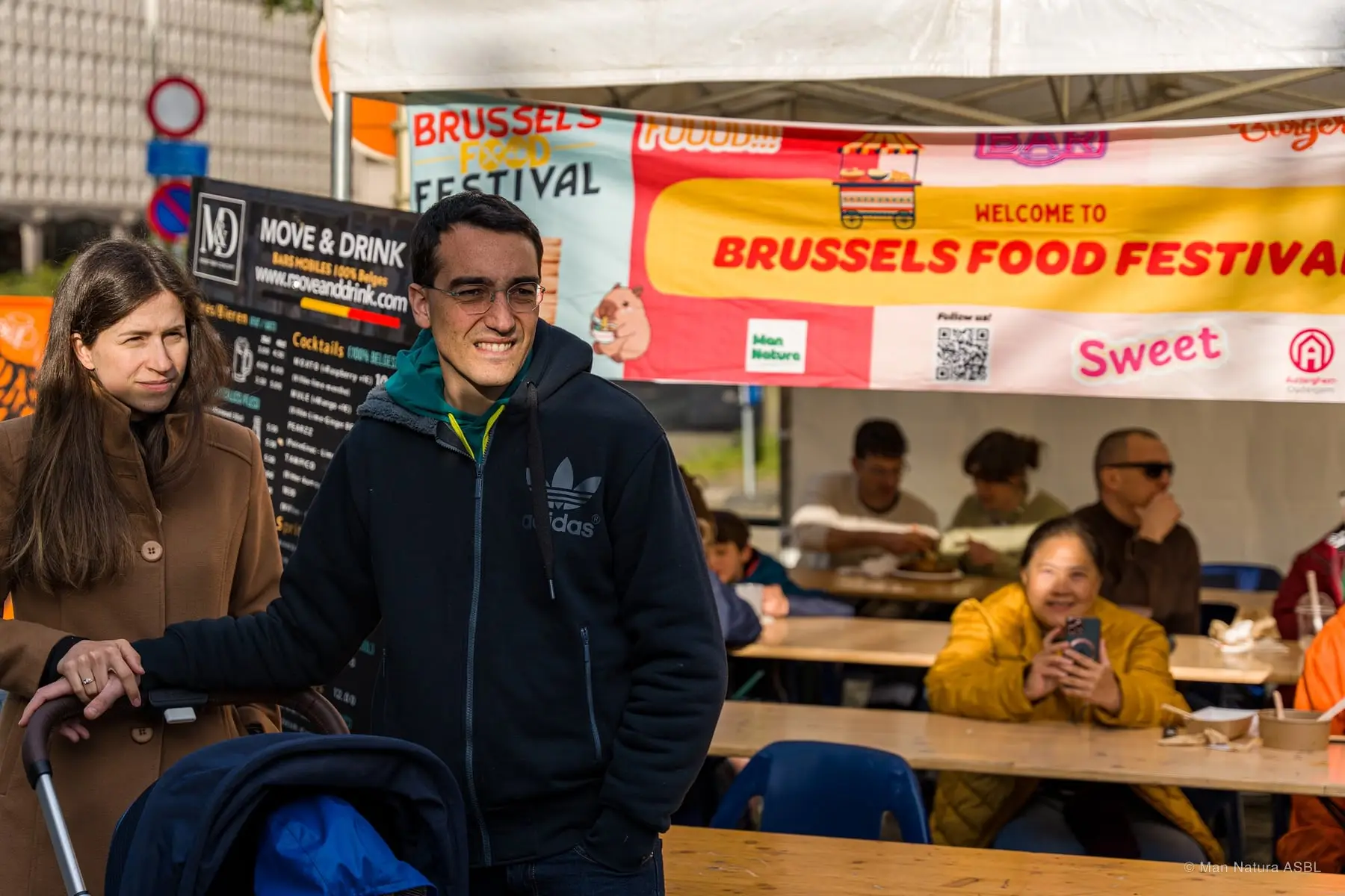 Un visiteur sourit devant la banderole Brussels Food Festival, tablées de convives à l'arrière-plan