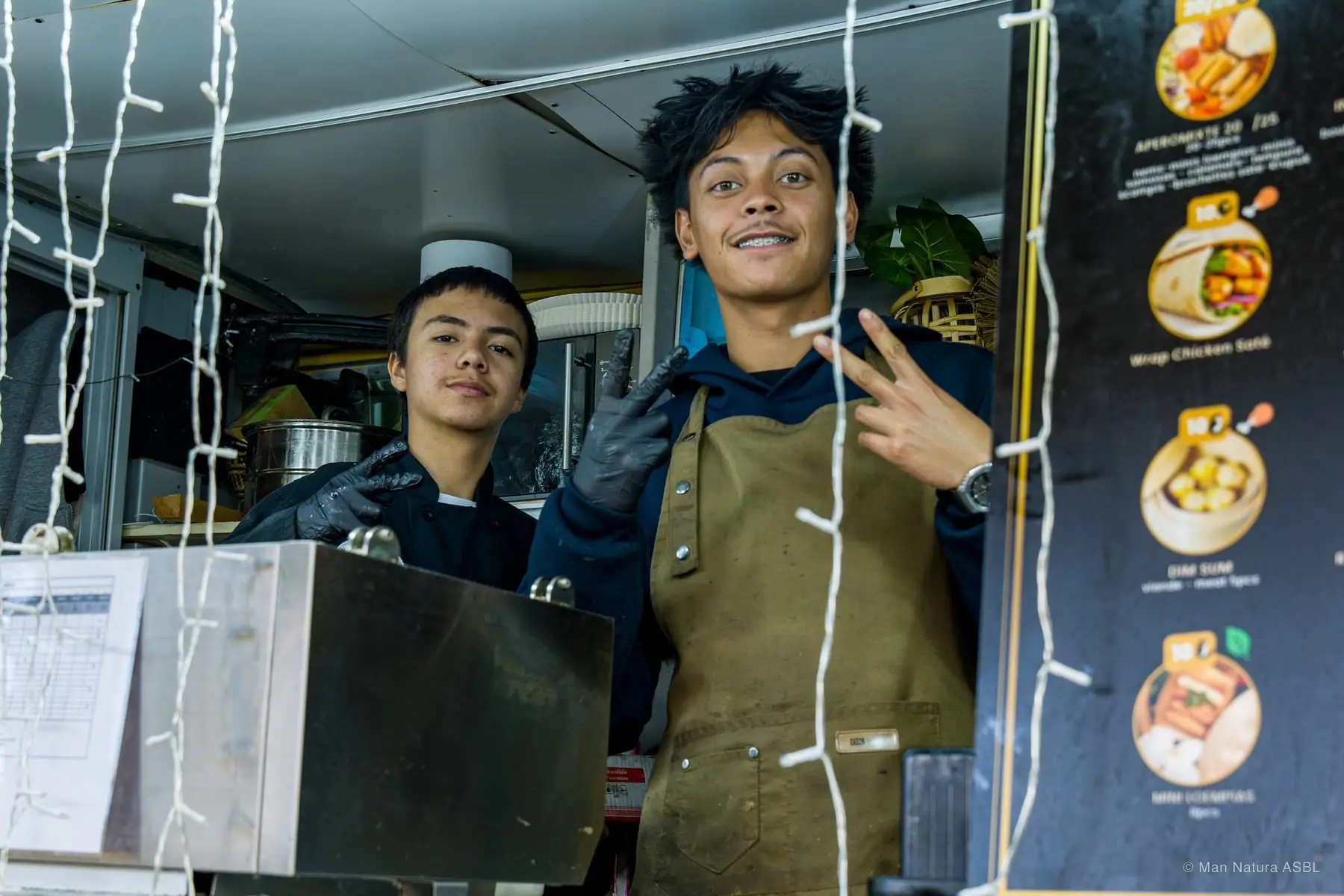 Deux cuisiniers en tablier posent devant leur comptoir décoré de guirlandes lumineuses
