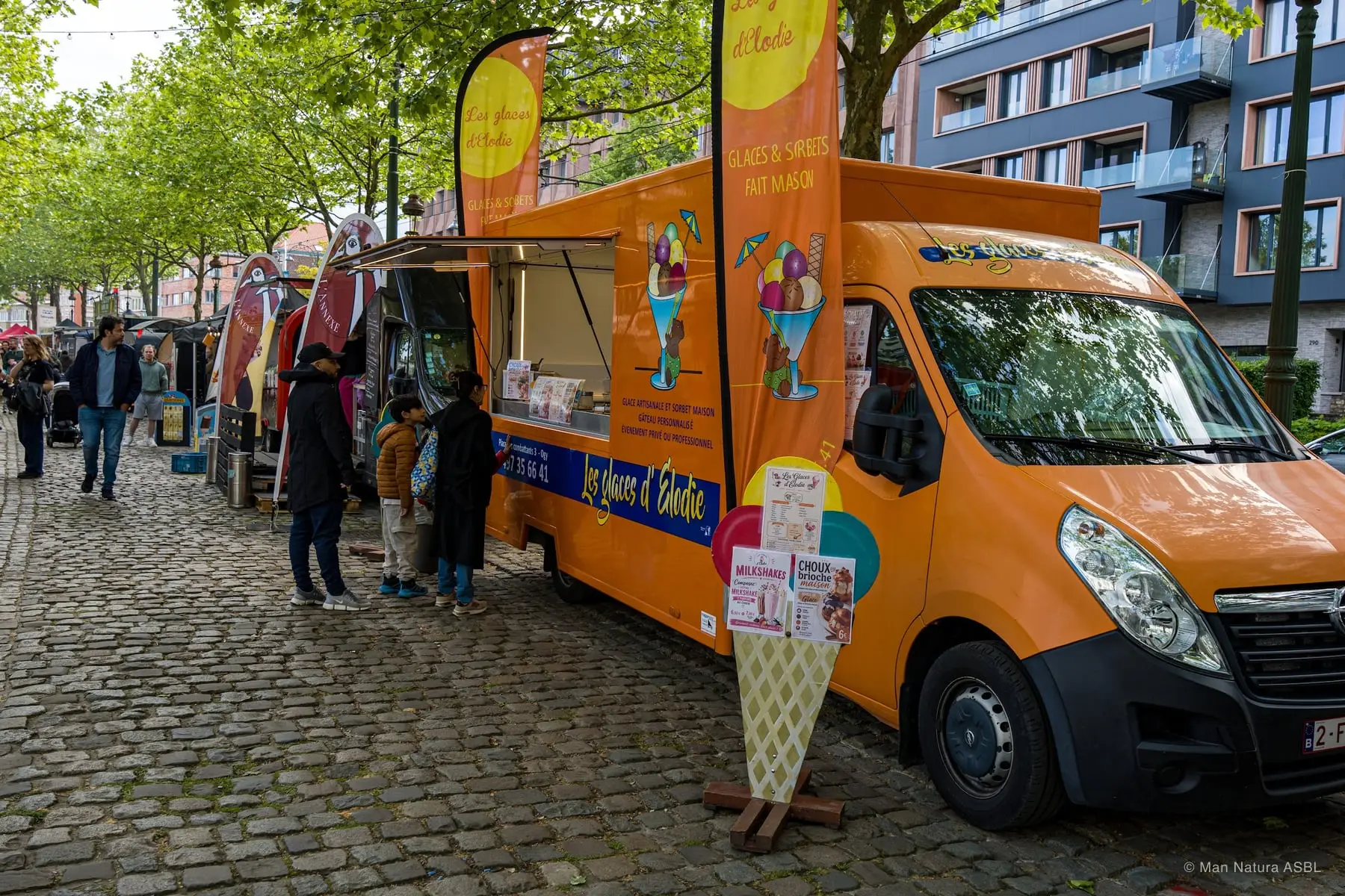 Camion à glaces orange garé le long de l'allée du festival, cornet géant en devanture
