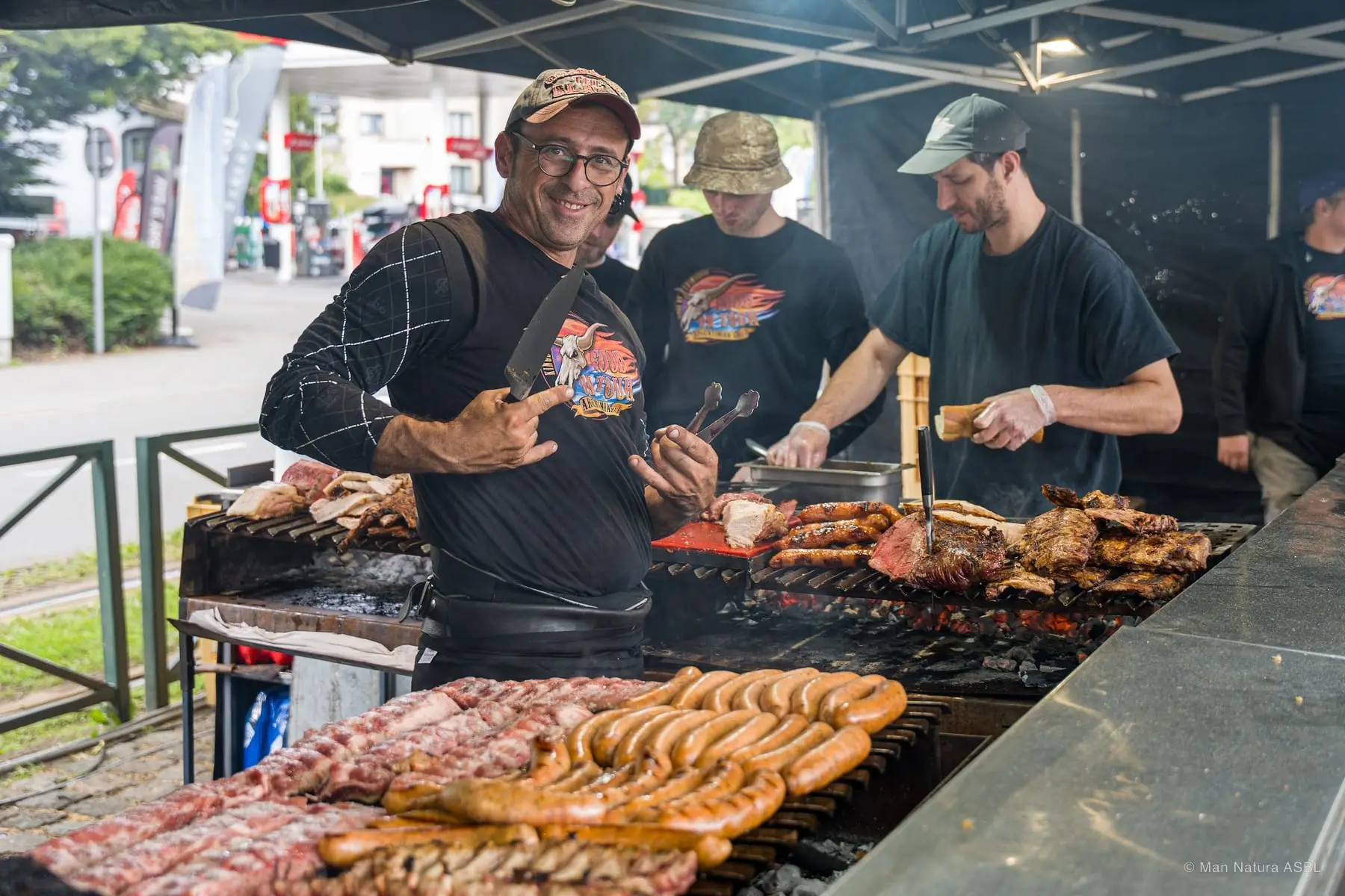 Grillades argentines : saucisses et pièces de viande sur un grand barbecue, trois cuisiniers au travail