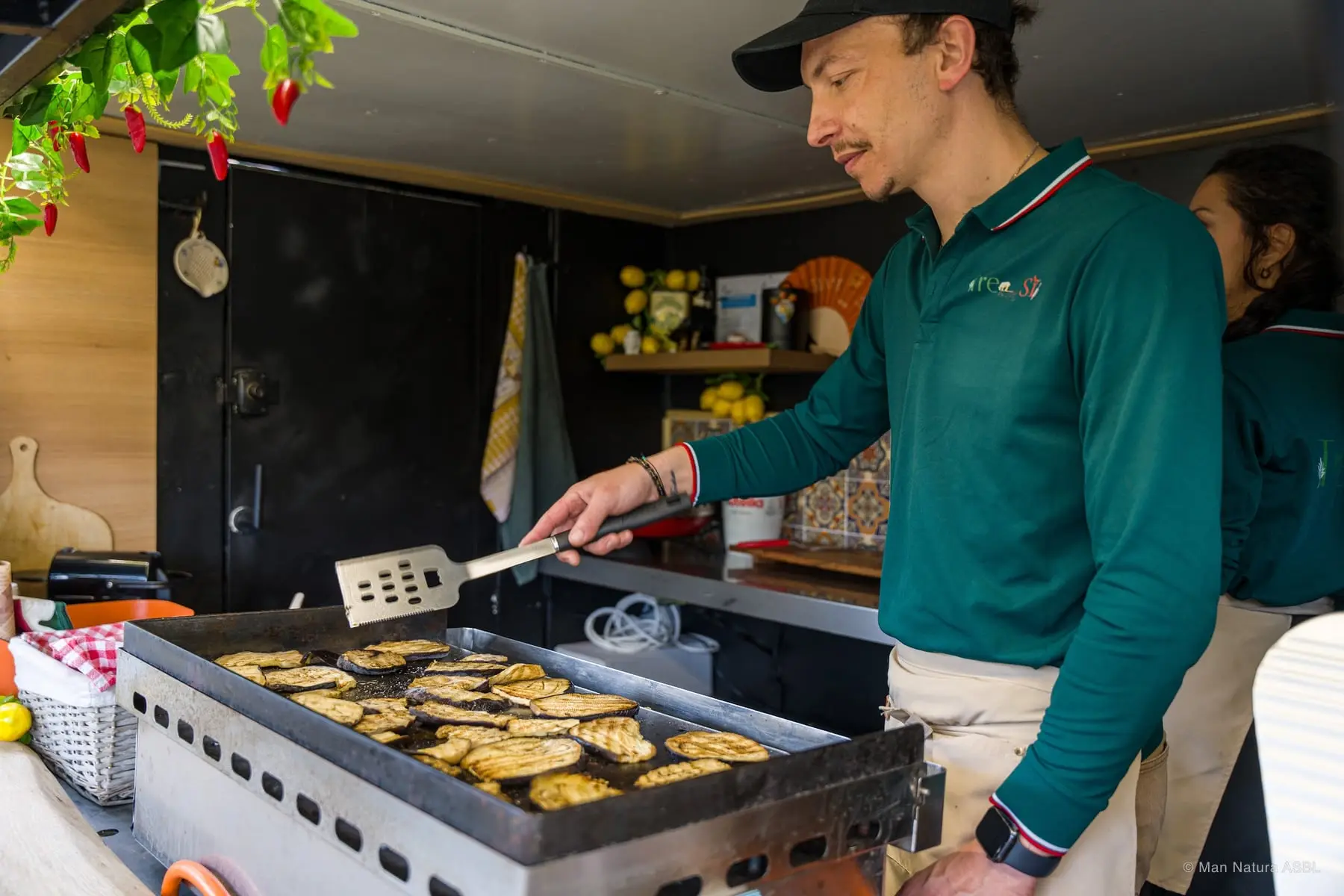 Un cuisinier retourne des aubergines grillées sur sa plancha dans le camion