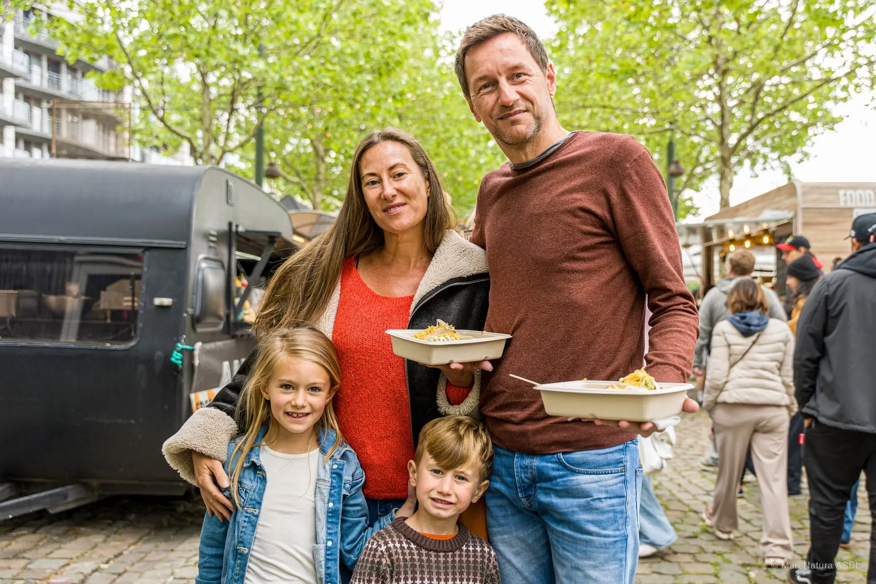 Une famille de quatre pose avec ses barquettes de pâtes devant un food truck