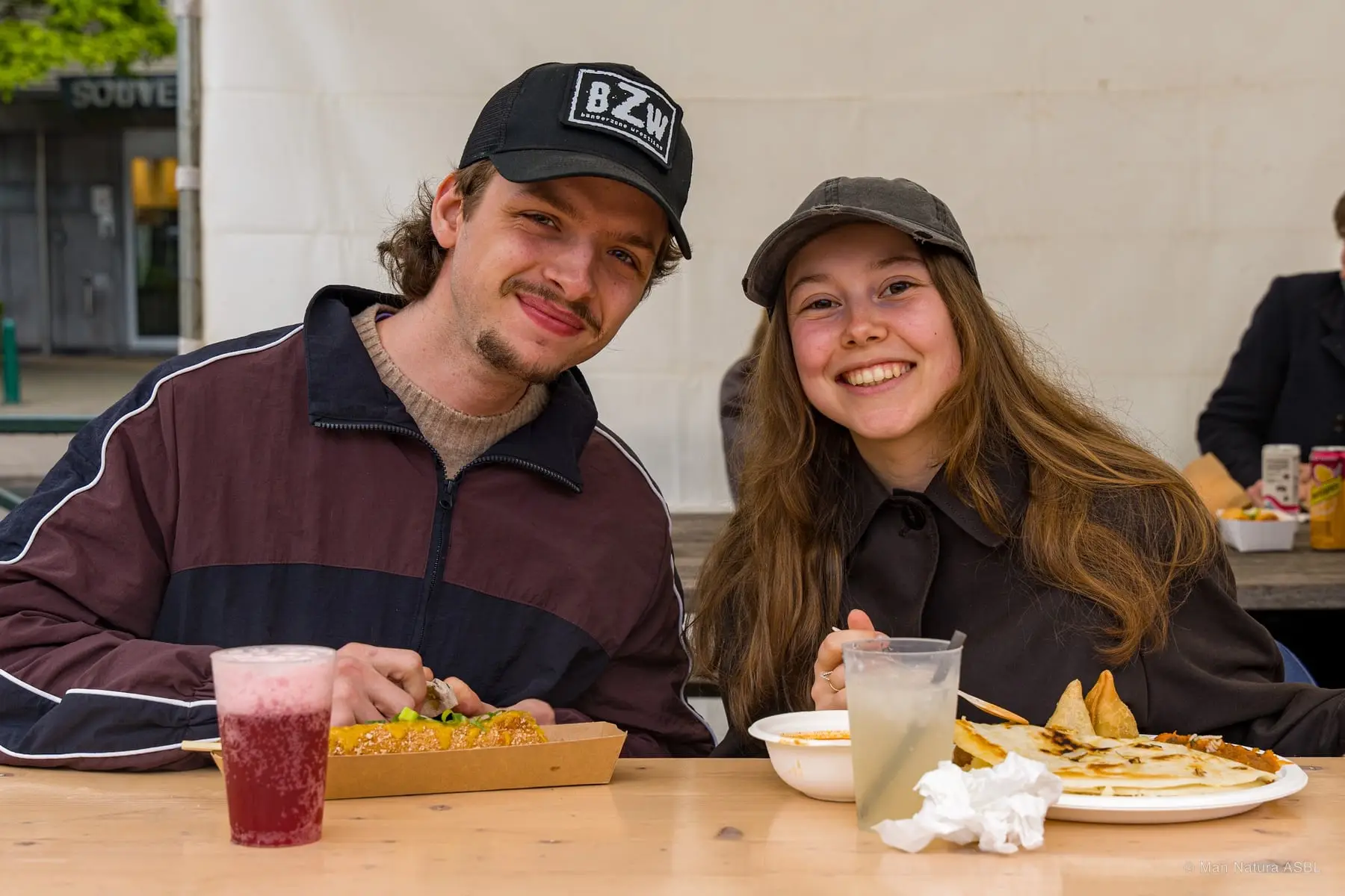 Un couple attablé devant ses plats et ses boissons, sourire à la caméra