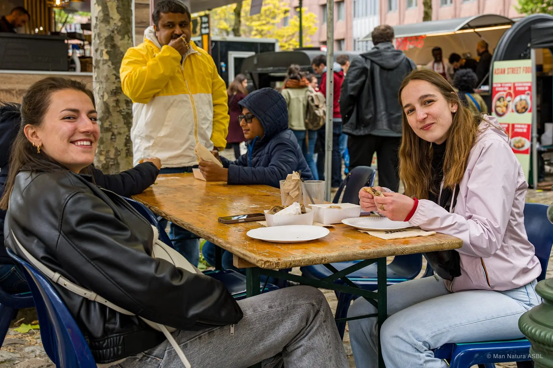 Trois amies partagent leur repas à une table en bois au cœur du festival