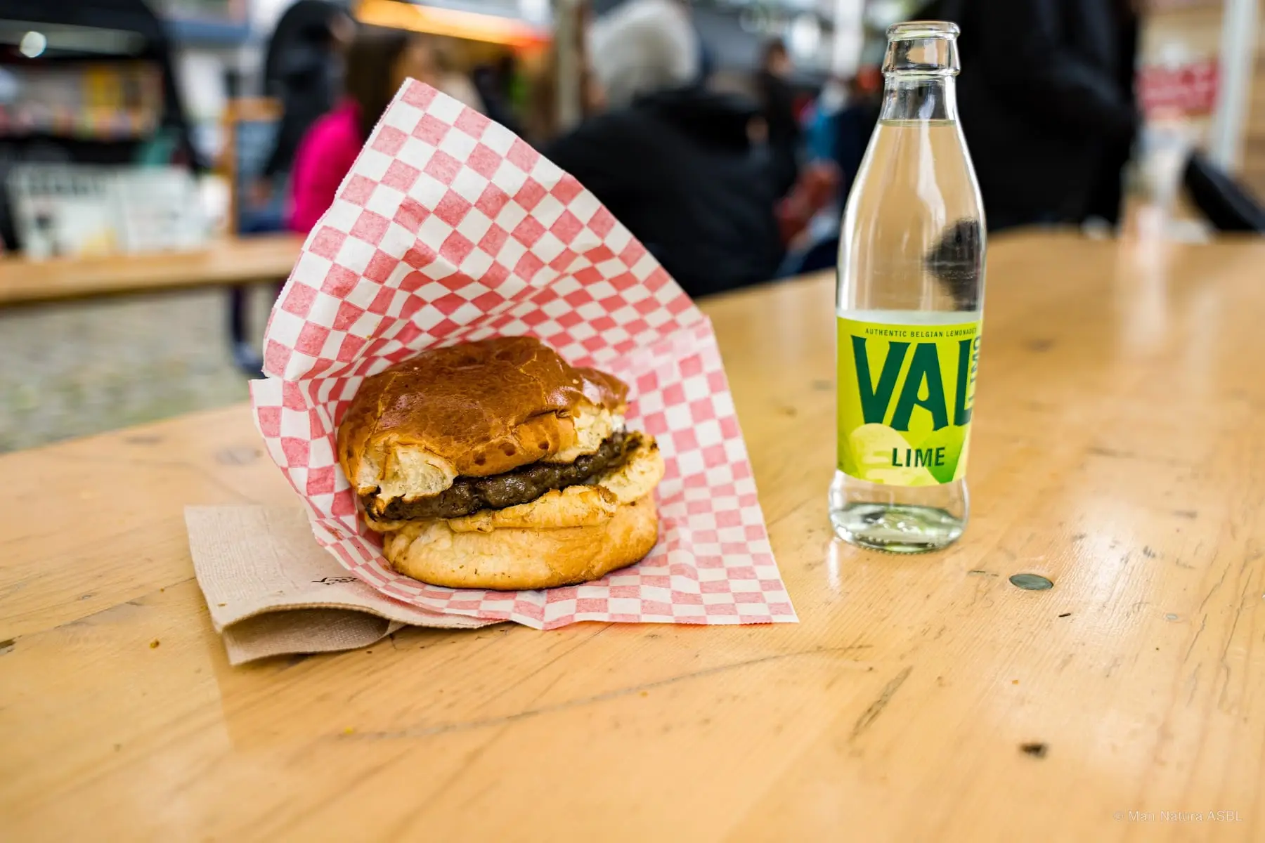 Burger servi dans son papier à carreaux avec une limonade, sur une table en bois