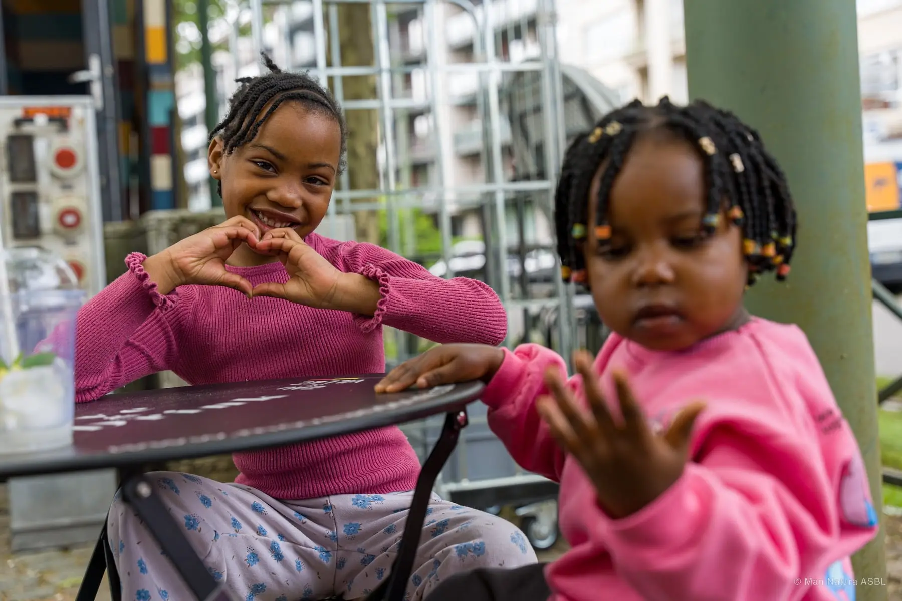 Une petite fille forme un cœur avec ses mains à côté d'une plus jeune enfant
