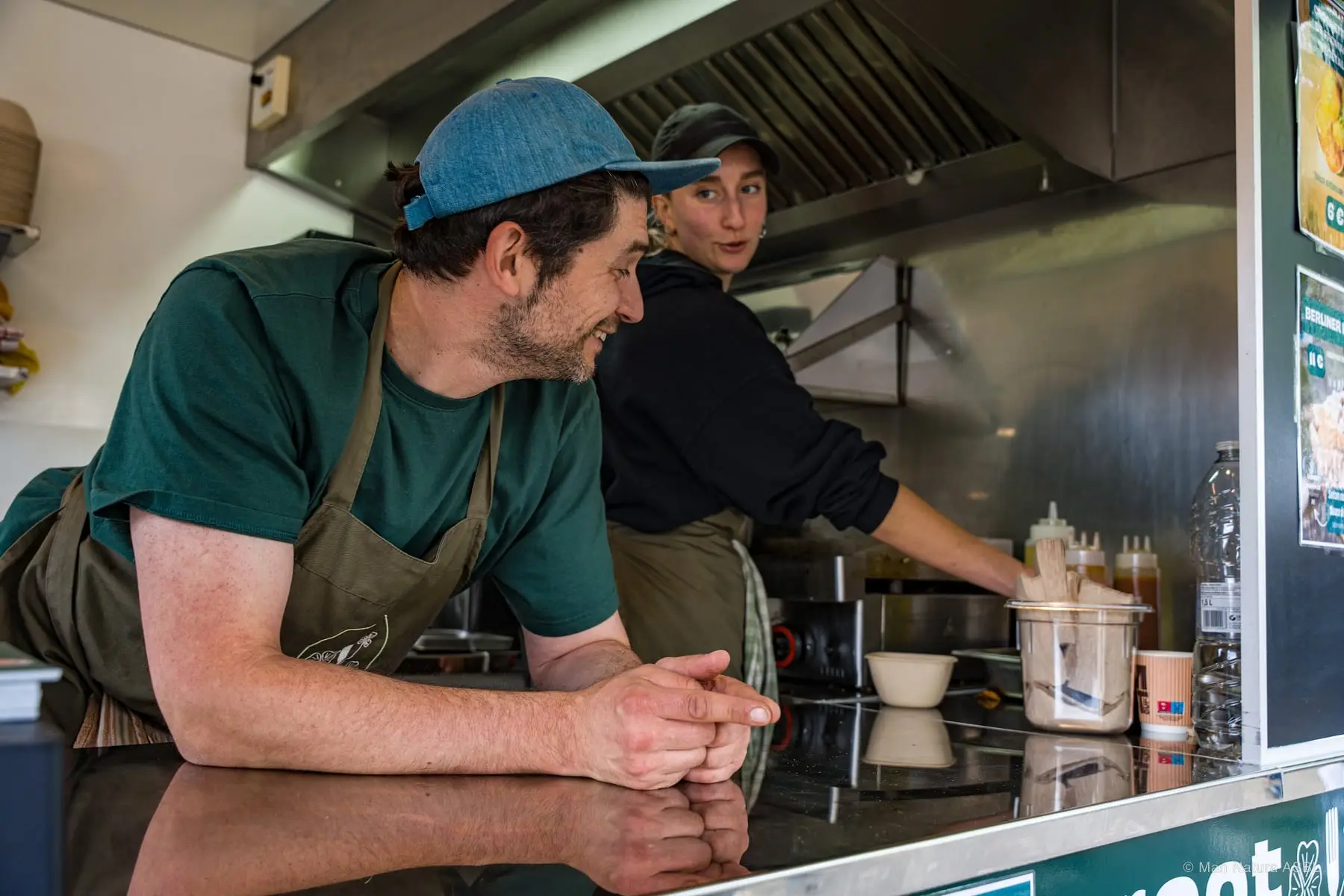 Deux cuisiniers en tablier vert s'accoudent au comptoir de leur camion
