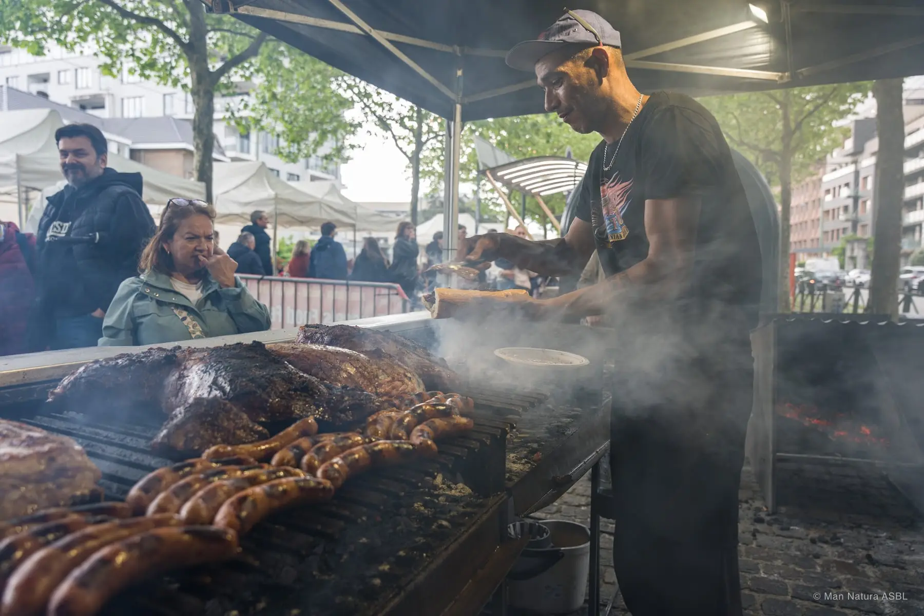 Le grill fume sous la tente, saucisses et viandes alignées devant le cuisinier