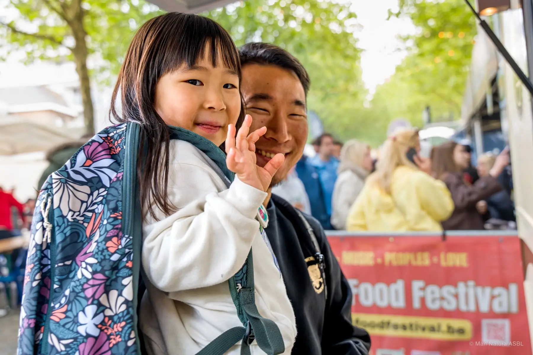 Un père porte sa fille sur les épaules devant la banderole du festival