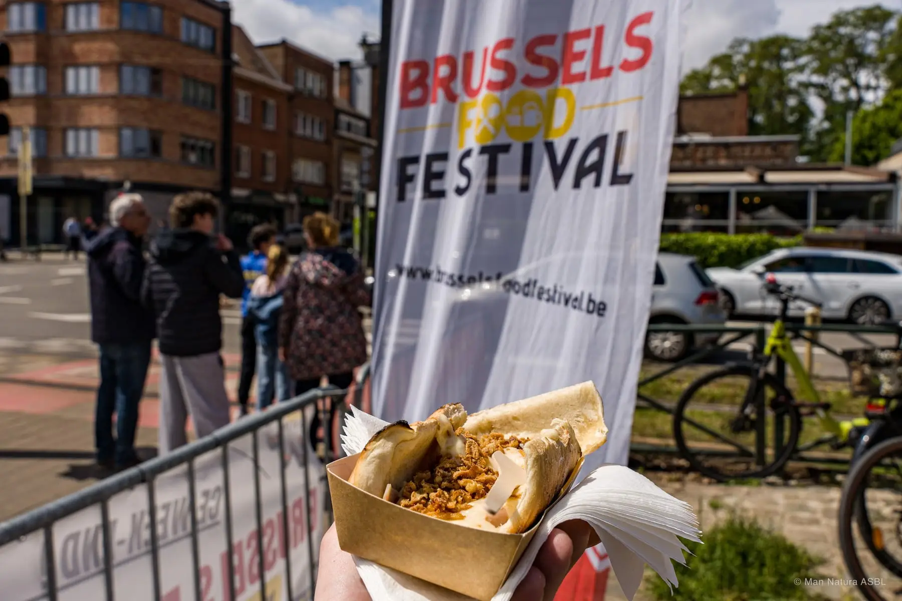 Une main tient sa barquette devant la banderole Brussels Food Festival